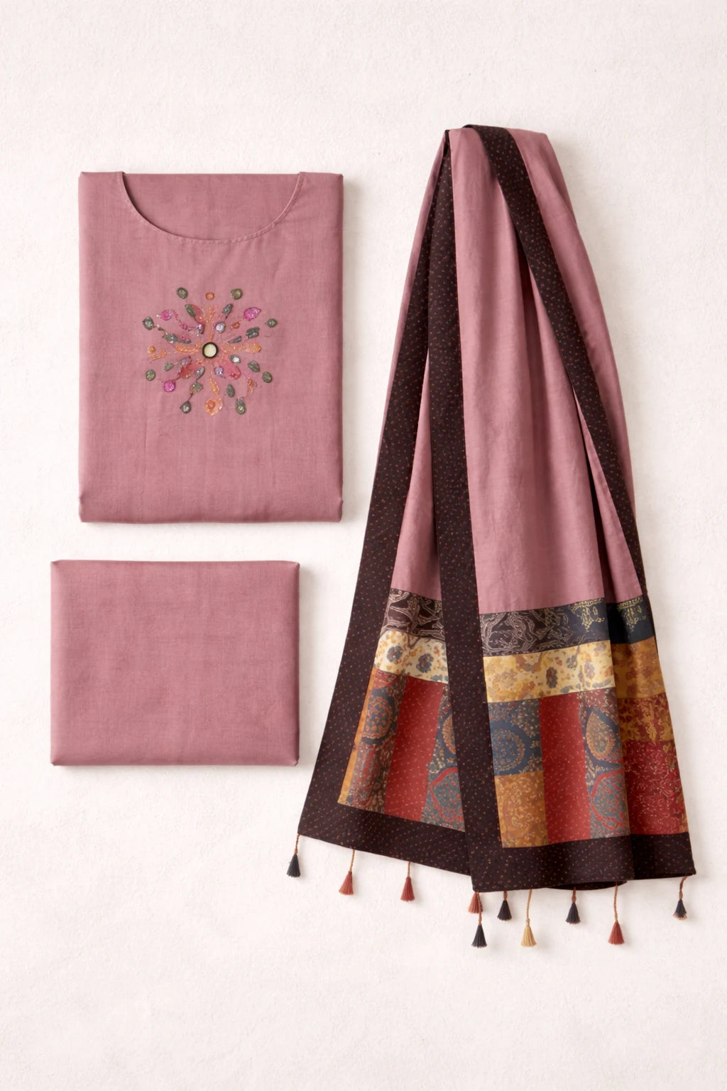 Pink fabric items with embroidery and a patterned scarf on a white background