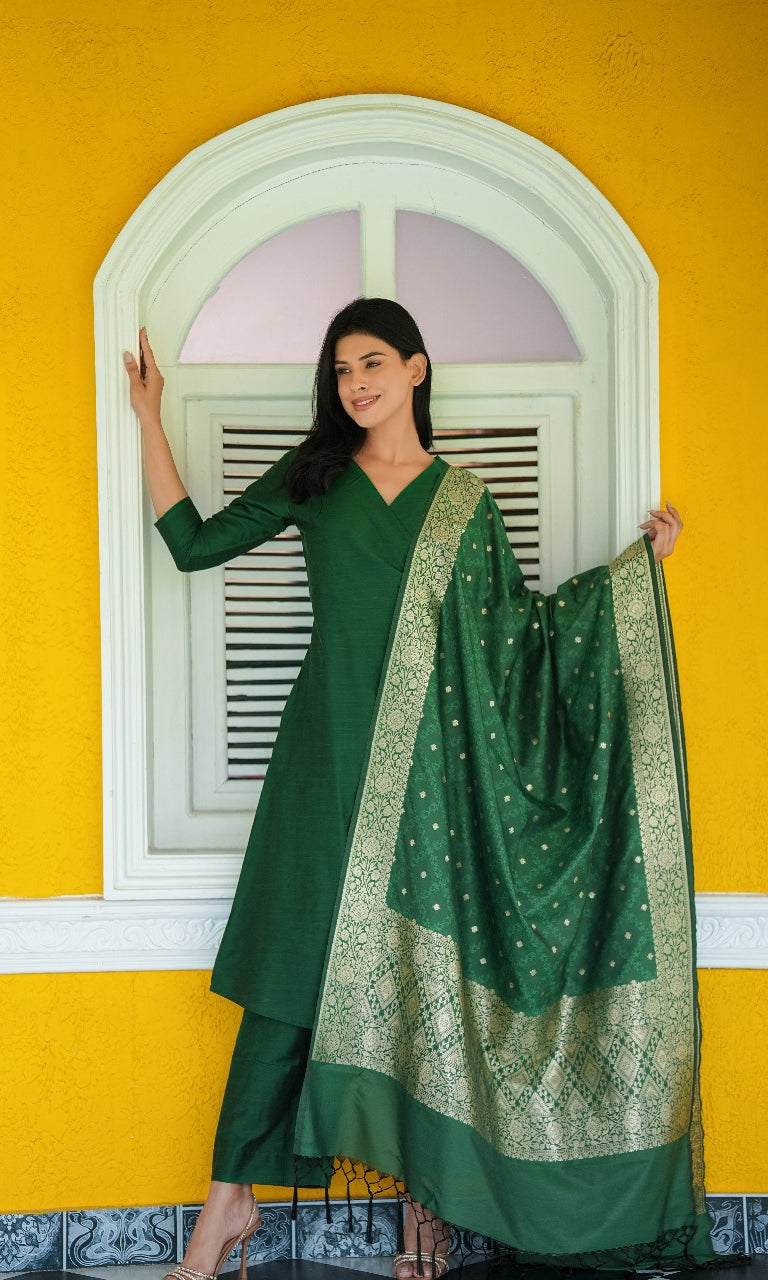 Woman in a green traditional outfit with a matching dupatta against a yellow wall.
