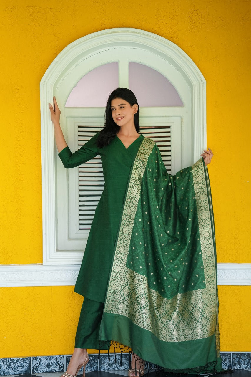 Woman in a green traditional outfit with a matching dupatta against a yellow wall.