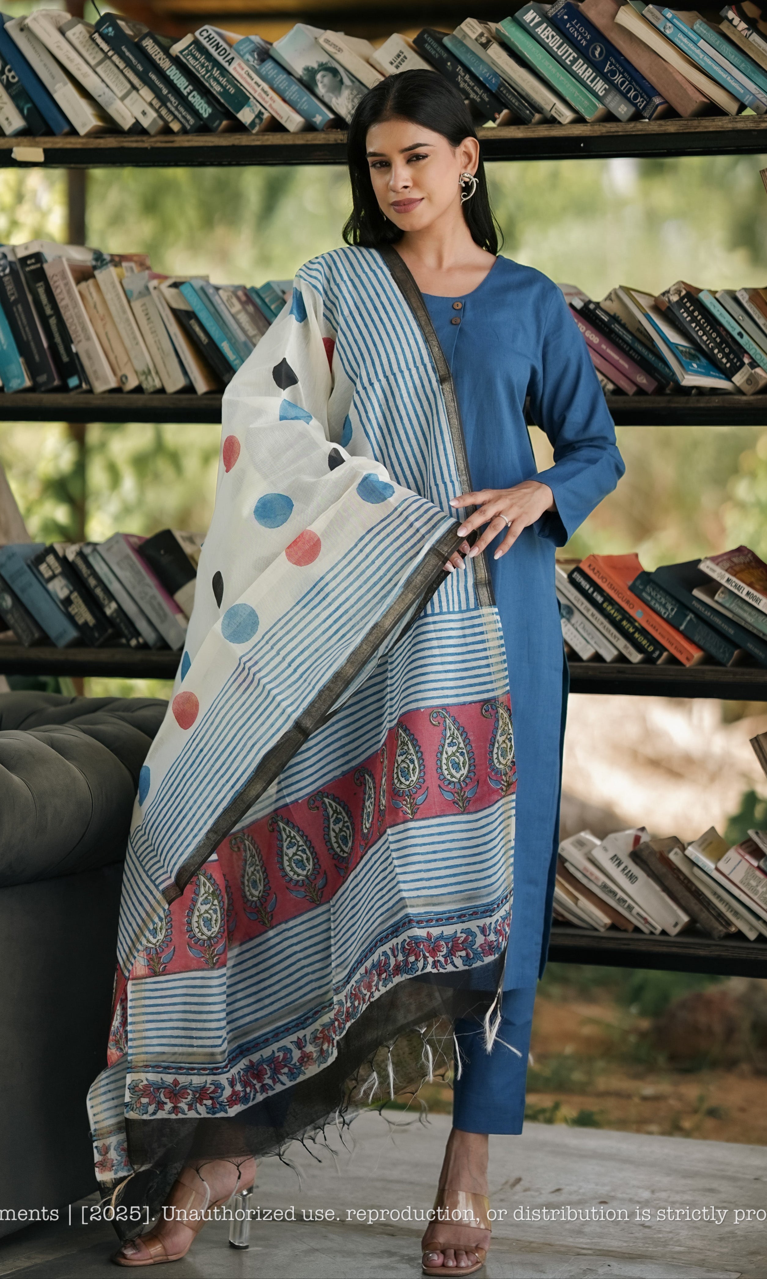 Woman holding a patterned fabric in front of a bookshelf