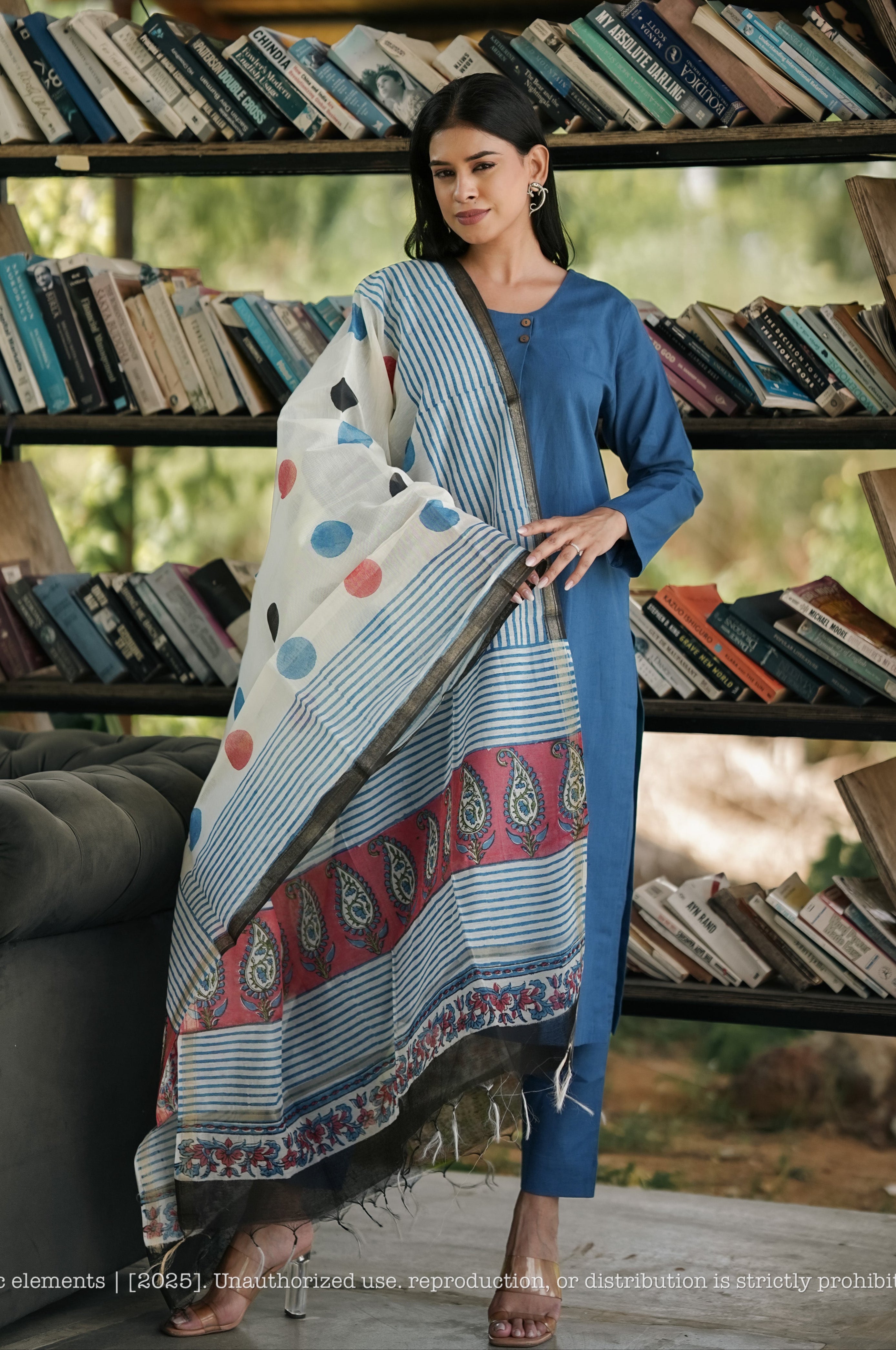 Woman holding a patterned fabric in front of a bookshelf