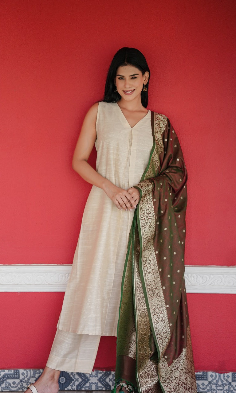 Woman in a white outfit with a brown and green patterned scarf against a red wall.