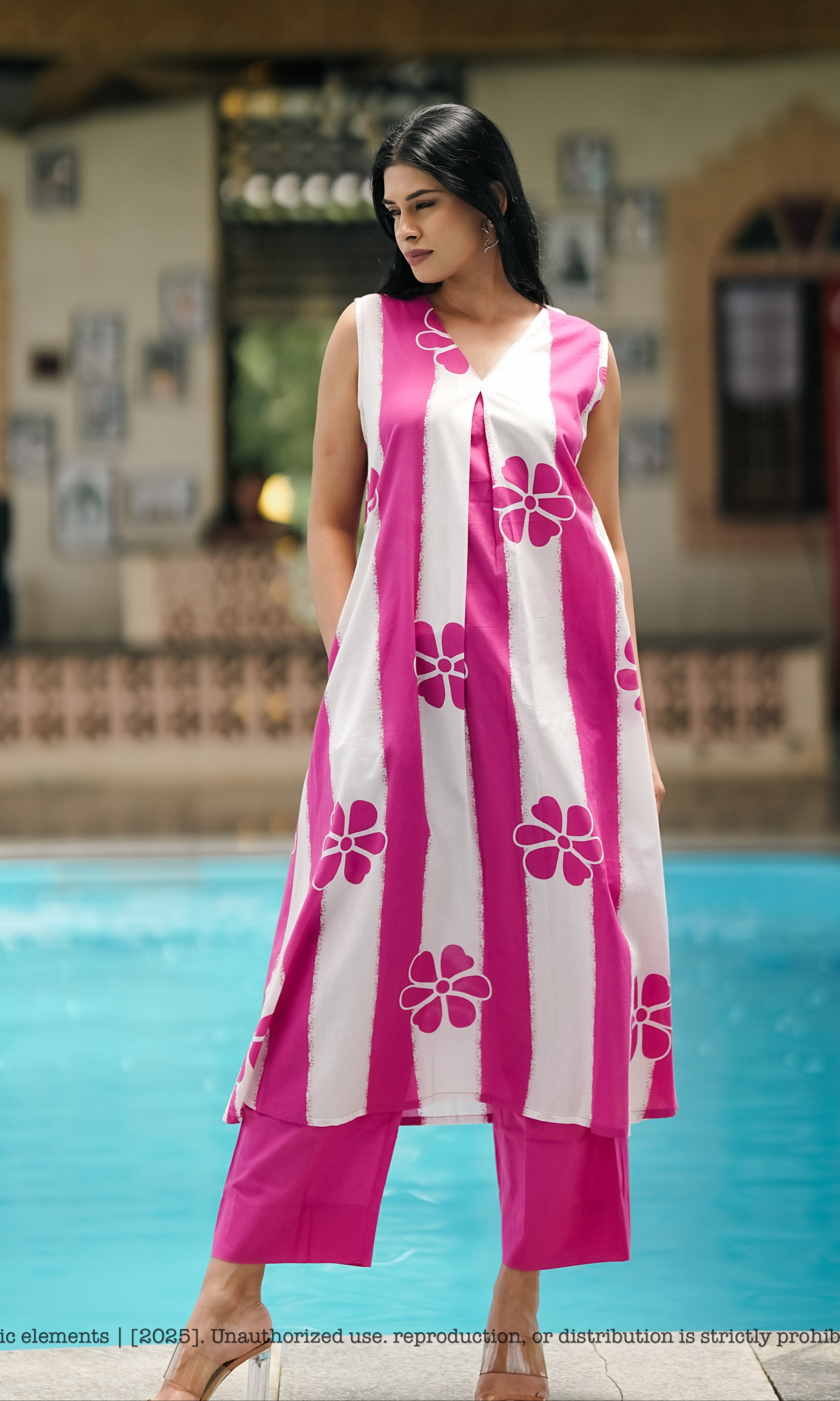 Woman in a pink and white floral dress standing by a pool.